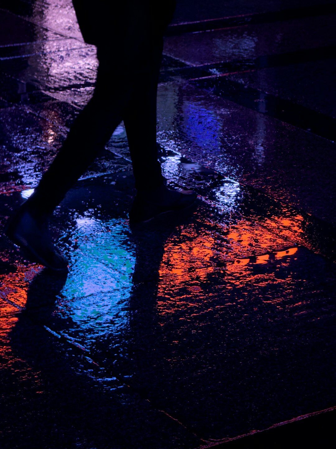 Anonymous silhouette of a person walking on a rainy city street at night